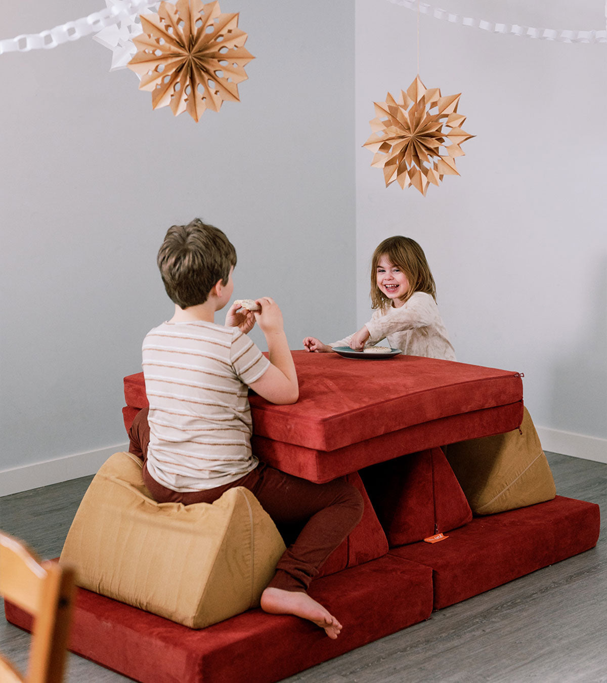 Two children sit at a "Nugget table" build made with Redwood and Sandcastle Nuggets, with two decorate stars suspended from the ceiling above.