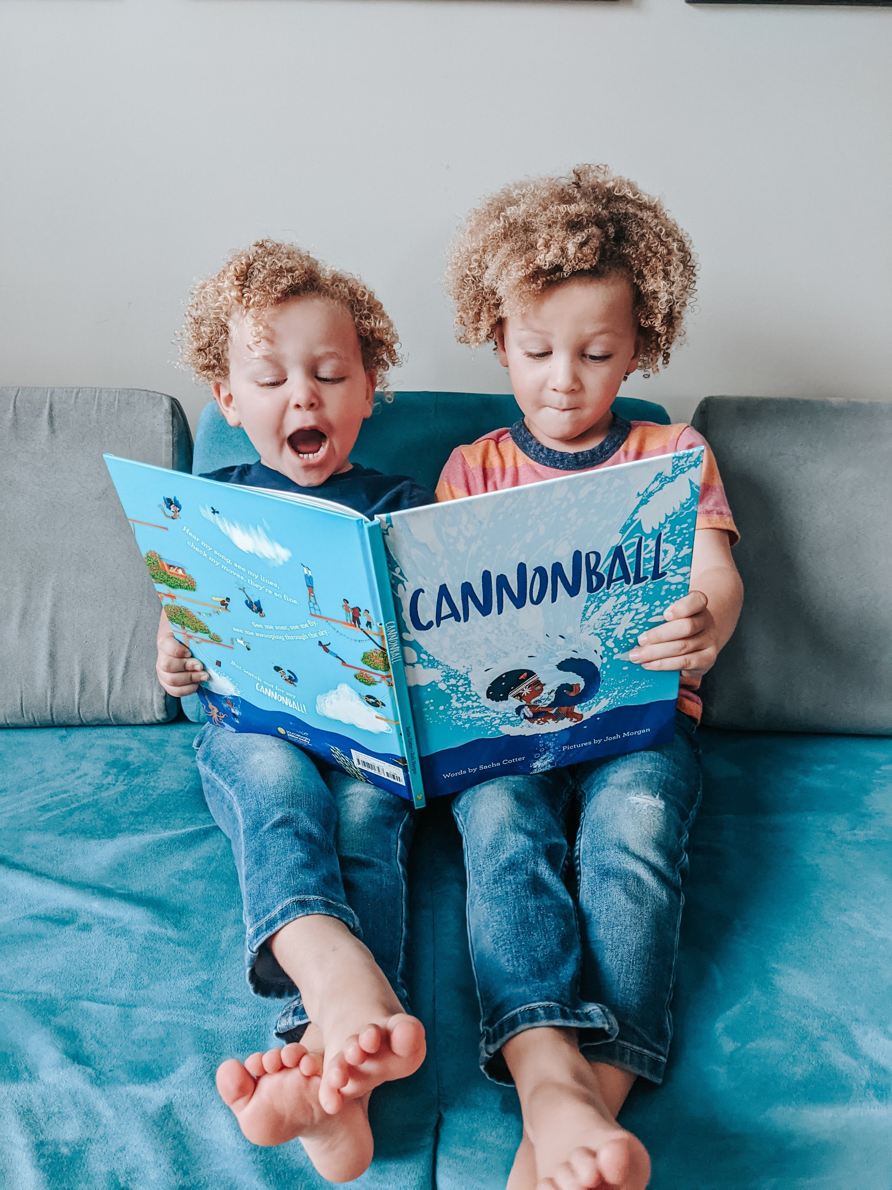 Two kids holding "Cannonball" on their laps, legs extended with ankles crossed, with Little Curly's mouth open like he's shouting "Cannonball!"