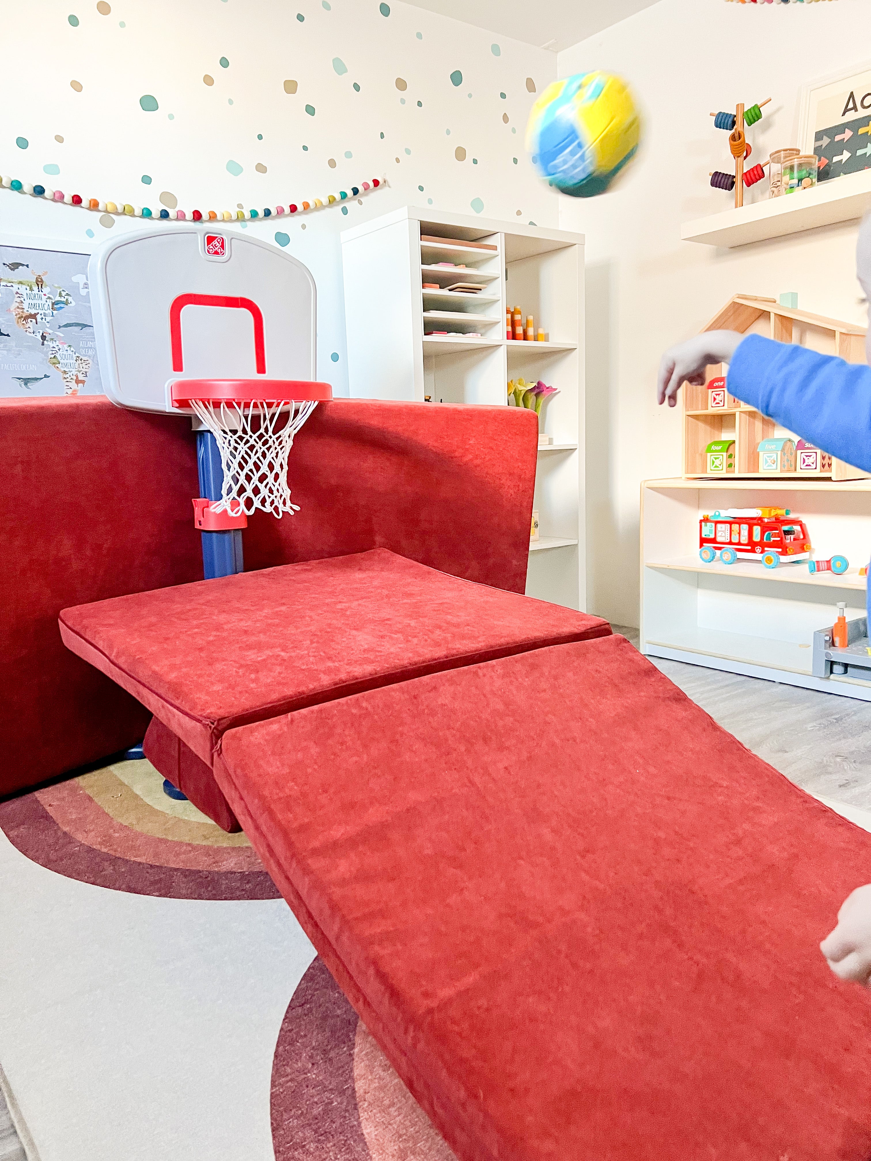 Child out of frame throws a basketball at the net, which is framed with a Nugget couch to roll the ball back to the player like an arcade basketball game.