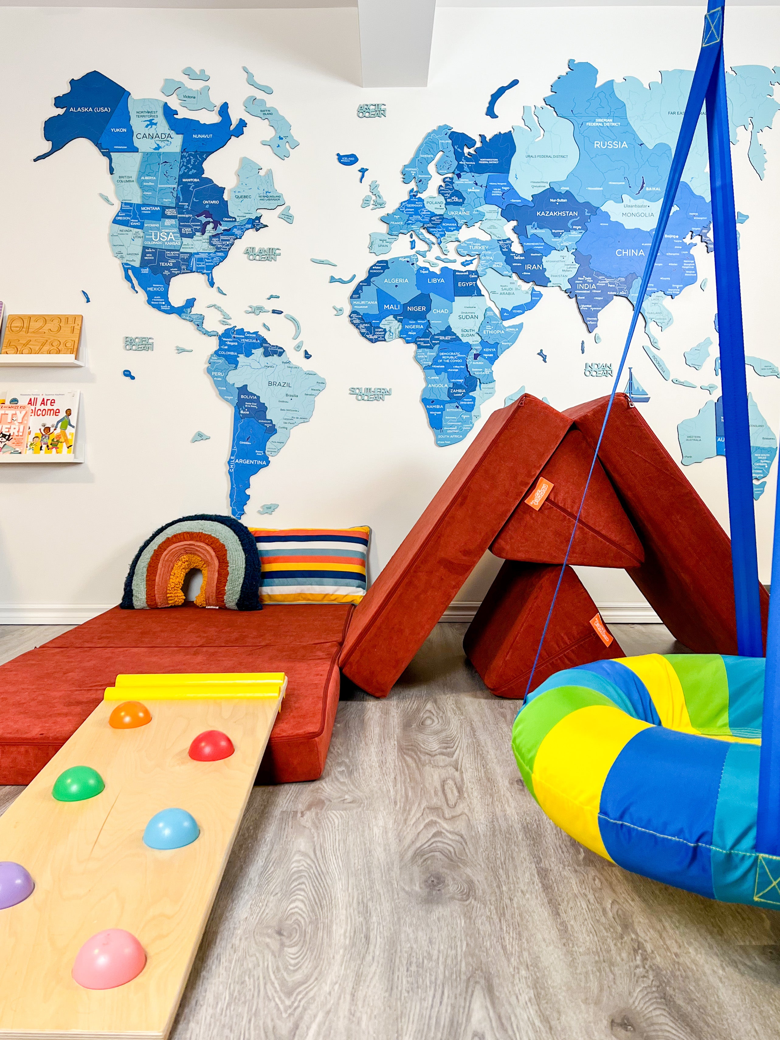 An indoor playground, complete with climbing ramp, swing, and Nugget build. A colorful world map is on the background wall.