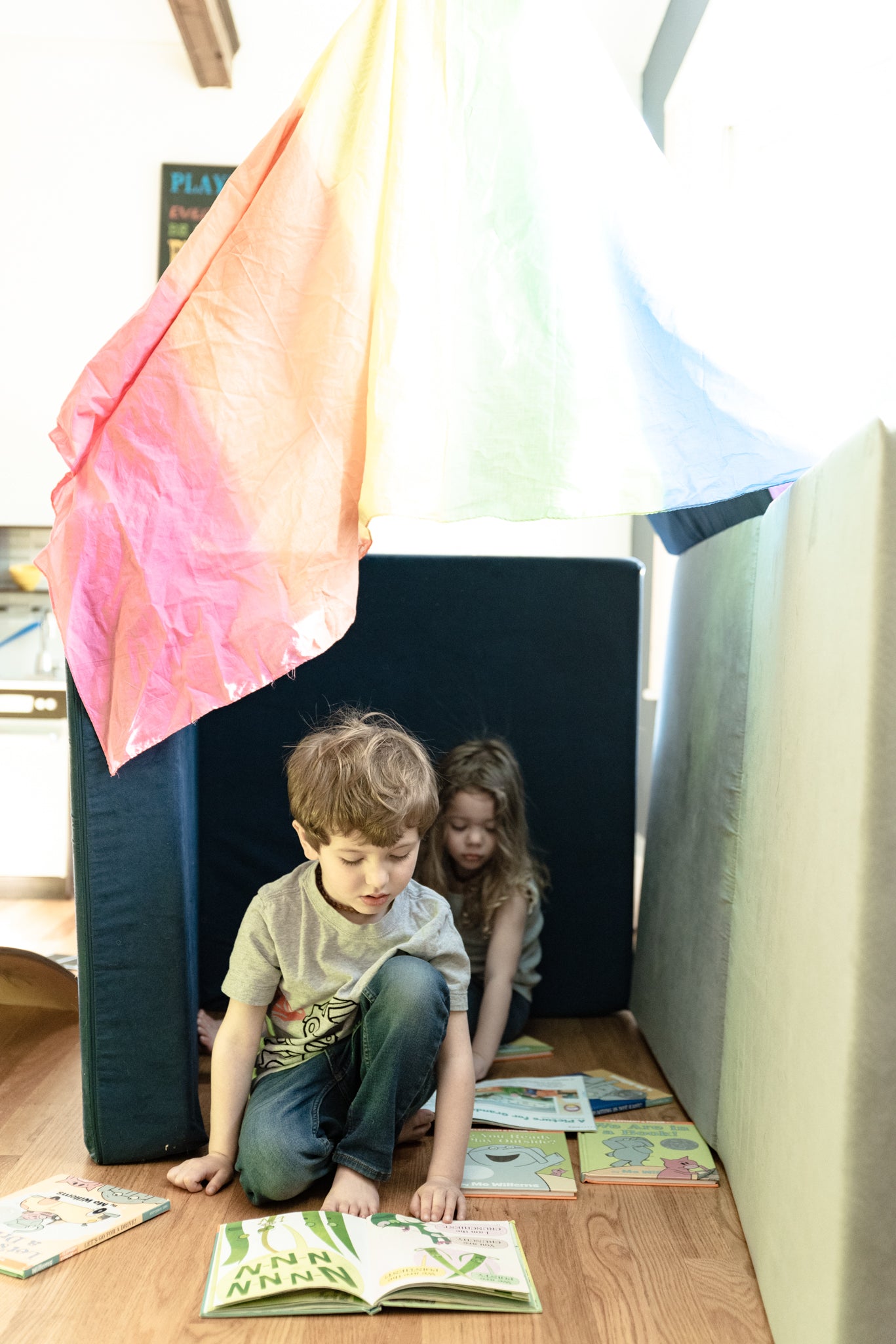 Two children reading stories in a Nugget fort, made with a play silk as the roof