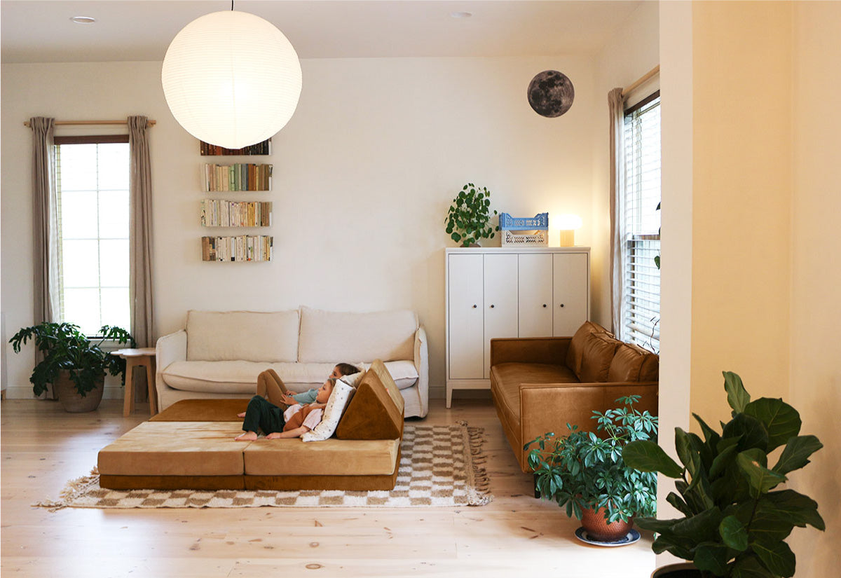 A brightly lit living room featuring a Bearhug and Sandcastle lounging couch, green plants, and a large circular light fixture.