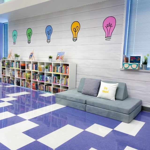 A gray Nugget in a classroom with white and purple checkerboard floor, a bookshelf, and colorful lightbulb images on wall.