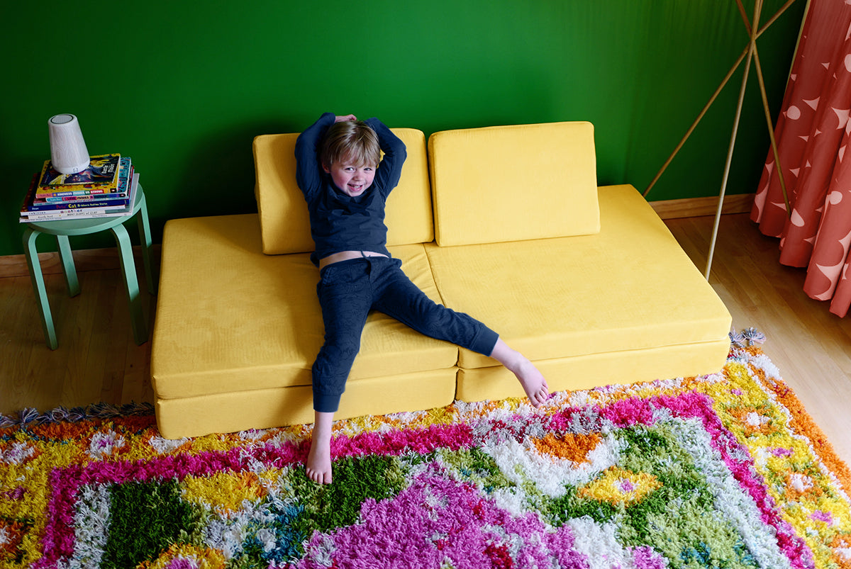 Child sits on a Nugget couch in Lemonade against a bright green wall