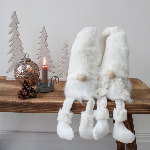 White plush gonk pair with dangly legs on wooden bench, with white trees, glittery baubles, dinner in chamberstick and natural pinecones