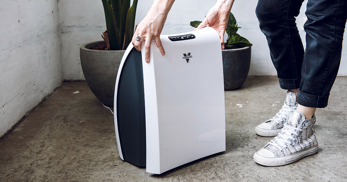 Image of woman wearing sparkly shoes and navy blue pants opening up a Vornado AC350 Air Purifier. 