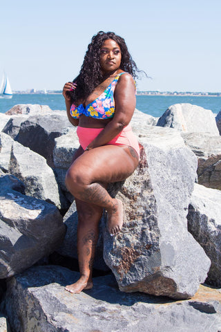 plus size model on the beach, ocean in the background laying on a large rock in a two piece swimsuit