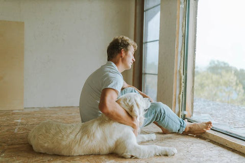A man sitting on the wooden floor with his white dog