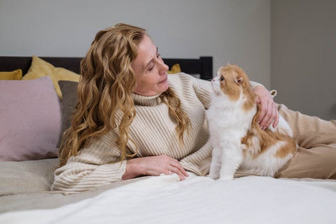 A blonde woman lying on a bed with her cat