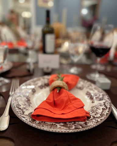 Thanksgiving place setting tablescape with Spode fine china and a bright orange linen napkin, with napkin ring and sprig of herb