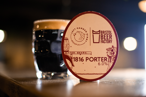 A dimpled pint mug with a dark porter beer and fluffy cream head stood next to an 1816 Porter pumpclip