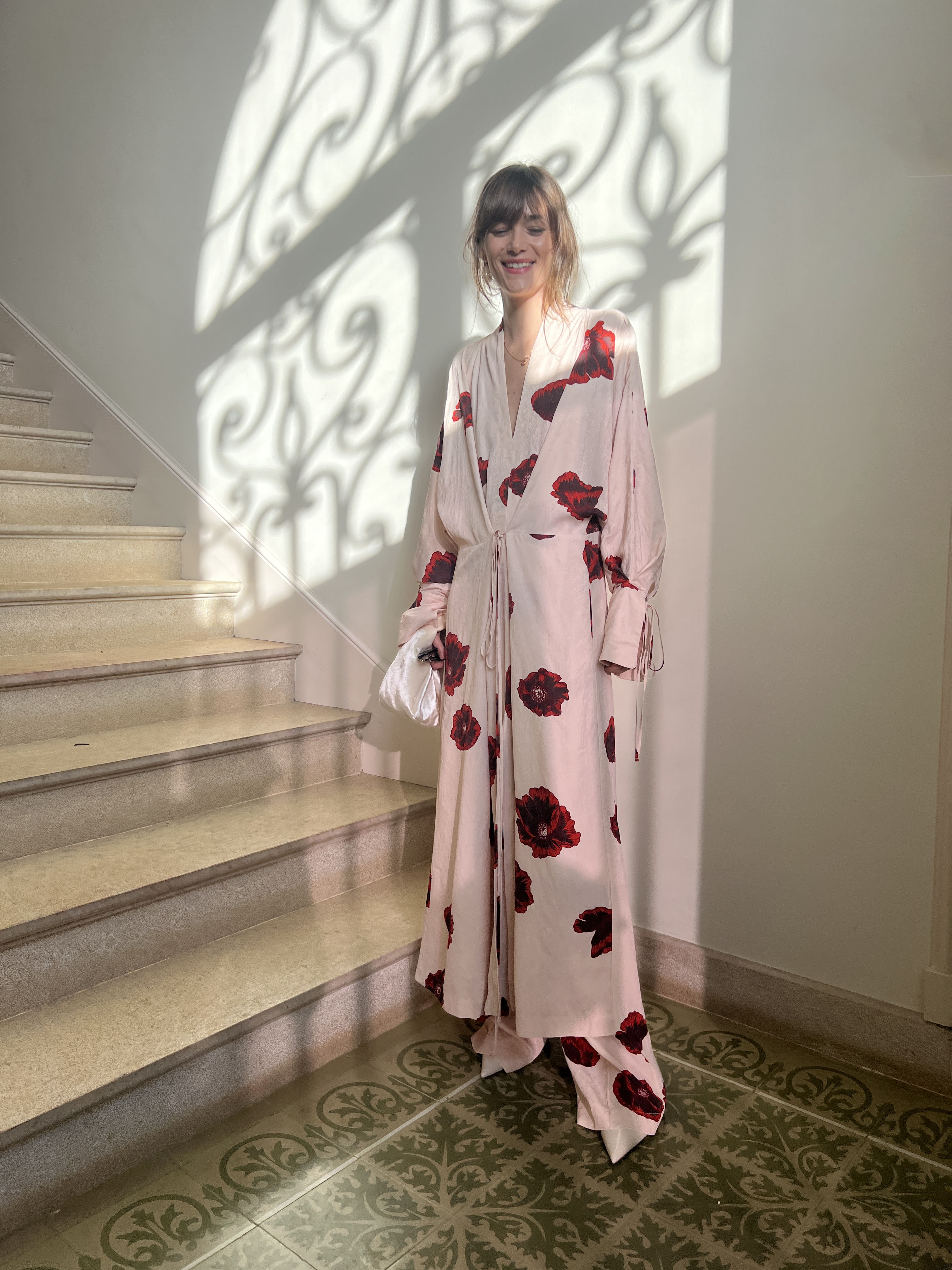Person in floral dress standing near stairs with patterned shadows on the wall.