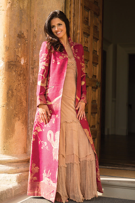 Woman with long brown hair in a pale pink maxi dress with deep pink long opera Devi coat in Deep Raspberry.