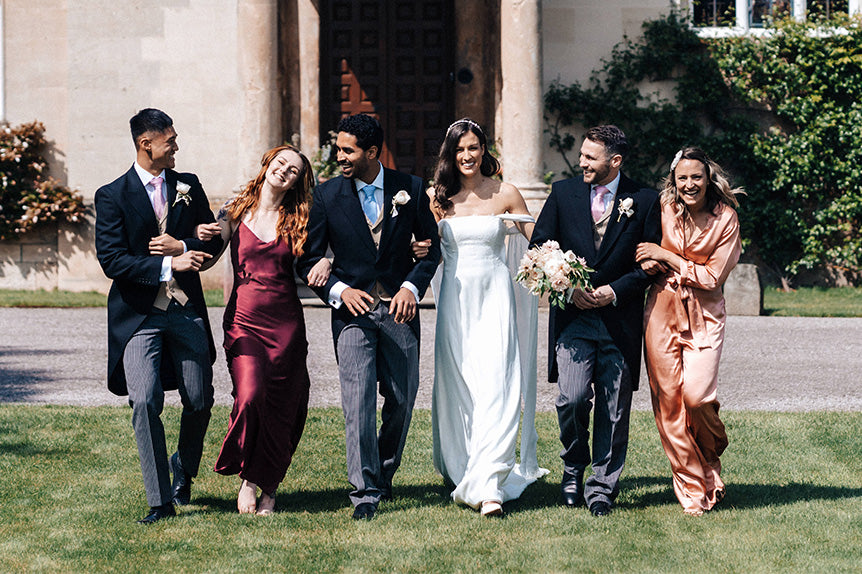 Wedding party walking outside with bridesmaids wearing cherry red silk slip dress and blush rose silk jumpsuit