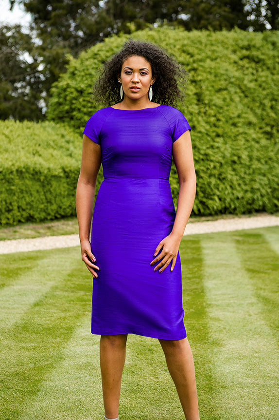 Black woman with curly hair standing on grass in violet purple hepburn dress