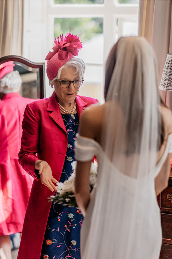 Mother of the bride seeing bride in her wedding dress, mother of the bride wears a blue dress and hot pink shibumi grace coat