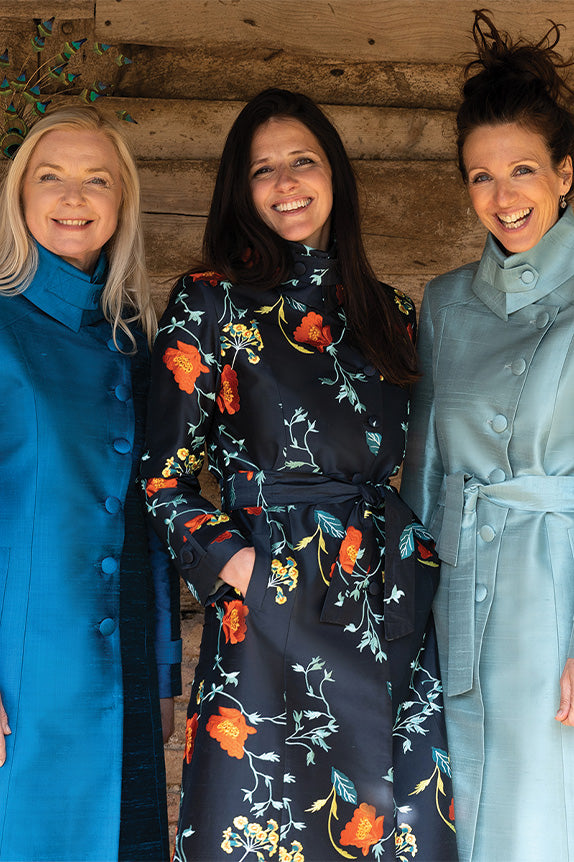 Three women of various ages wear silk trench coats