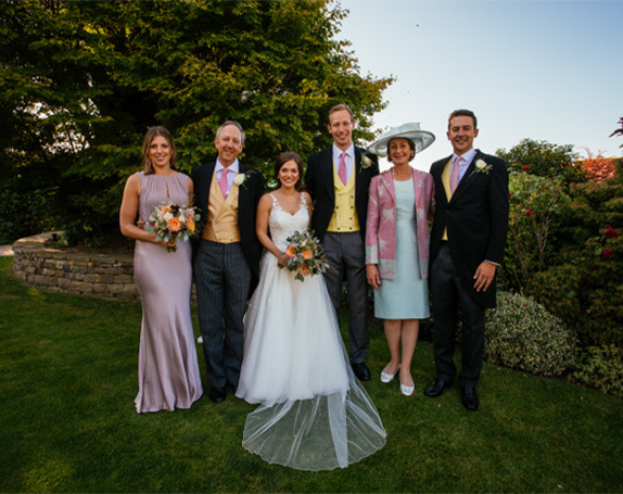 bridal party with bride, groom, and family, mother of the groom wears a classic blazer in pink