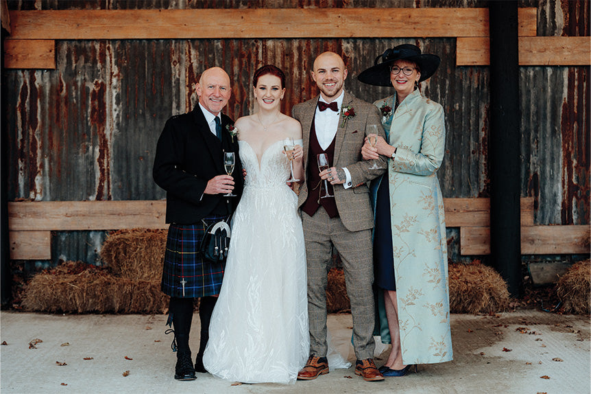 Wedding group with bride and groom with brides parents. Mother of the bride outfit has a blue embroidered long silk coat, Devi coat in Narnia.