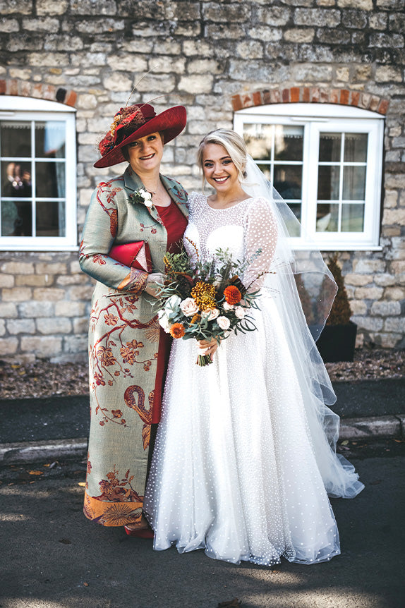 bride and mother of the bride with bride wearing aquila coat in opaline with red hat