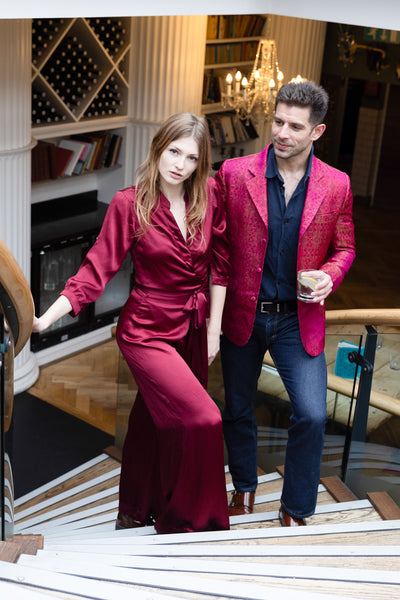 couple at the party, the women is wearing long silk red jumpsuit and the man is wearing silk pink jacket