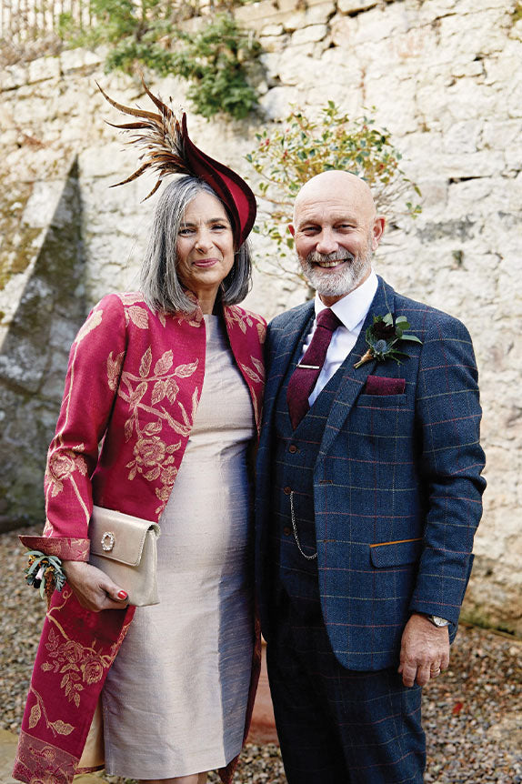 mature couple at wedding, man in blue tween suit and woman in deep raspberry knee length cashmere jacket lyra