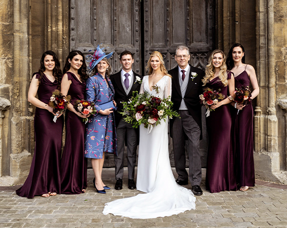 Bridal party with 4 bridesmaids, bride, groom and mother and father of the groom with mother of the groom wearing blue lyra coat