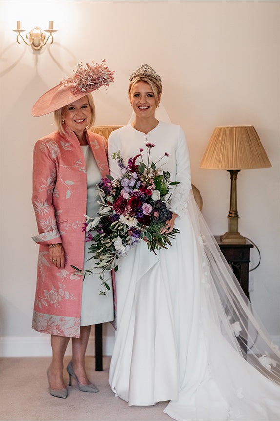 Bride and mother of the bride in shibumi lyra coat in rococo pink with har and blue dress