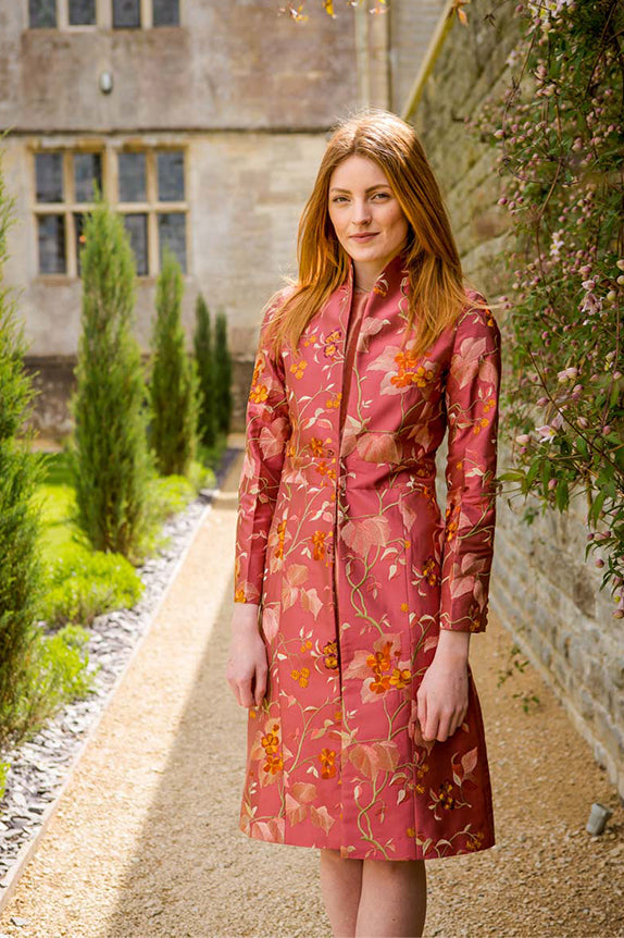 redhead woman standing in walled garden in blush pink embroidered coat