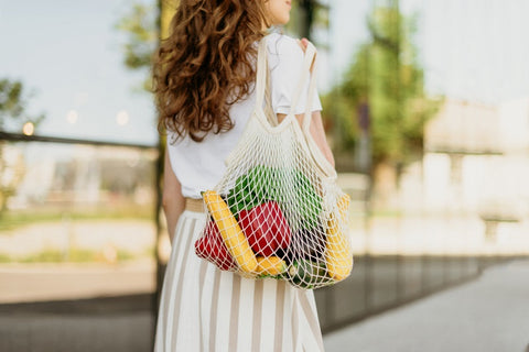 Woman holding reusable mesh shopping bags with vegetables