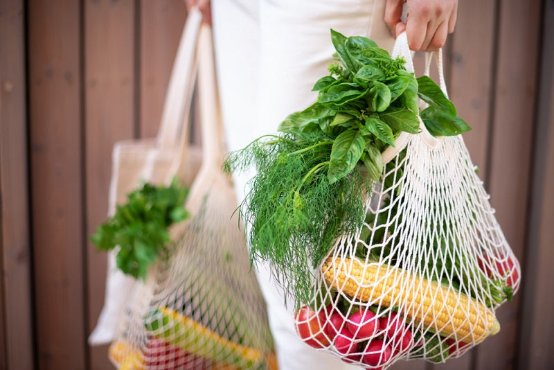Woman holding cotton shopper and reusable mesh shopping bags with vegetables