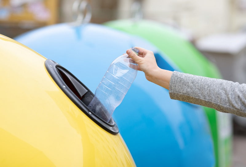 lady throwing plastic bottle into yellow recycle bin container outdoors