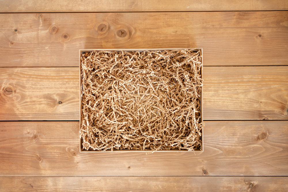 Opened gift box with shredded paper on wooden background