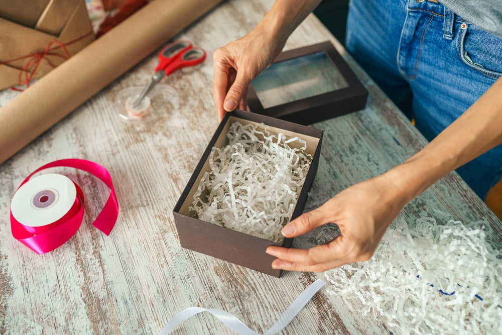 Woman putting kraft shredded paper in packaging box wrapping gift