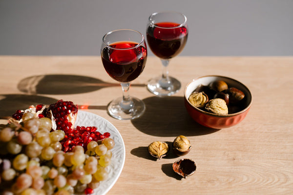 Dos copas de vino tinto junto a plato de frutas y nueces