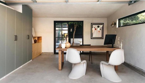 A room with a set of white chairs, a wooden desk, and black steel doors.