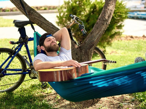 Man sleeping on a hammock holding a guitar