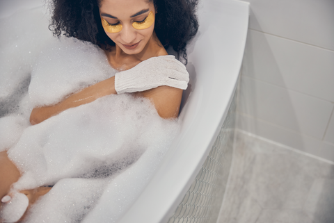 Woman in bathtub using exfoliating gloves on arm