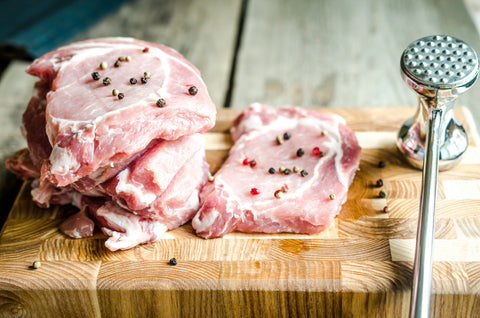 Pork on wooden board with meat tenderizer