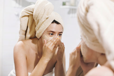 woman using face scrub while looking in the mirror