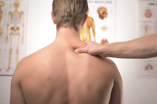 A man has is bare back facing the camera  in front of him doctor office images of the human body.  A doctor is examining  him.