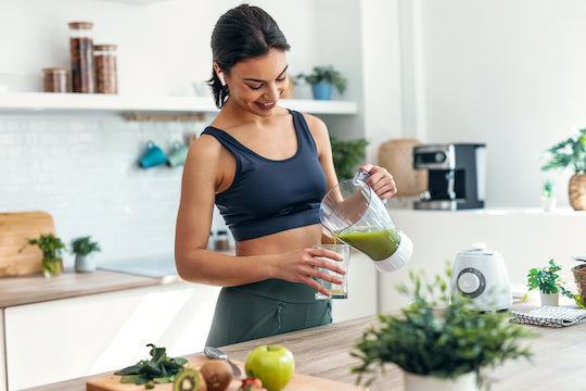 woman in kitchen, pouring a green smoothie