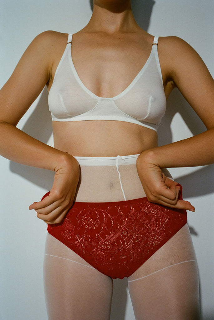 A model wearing the Briar Bralette in White and the Tris lace panty in red over white tights.