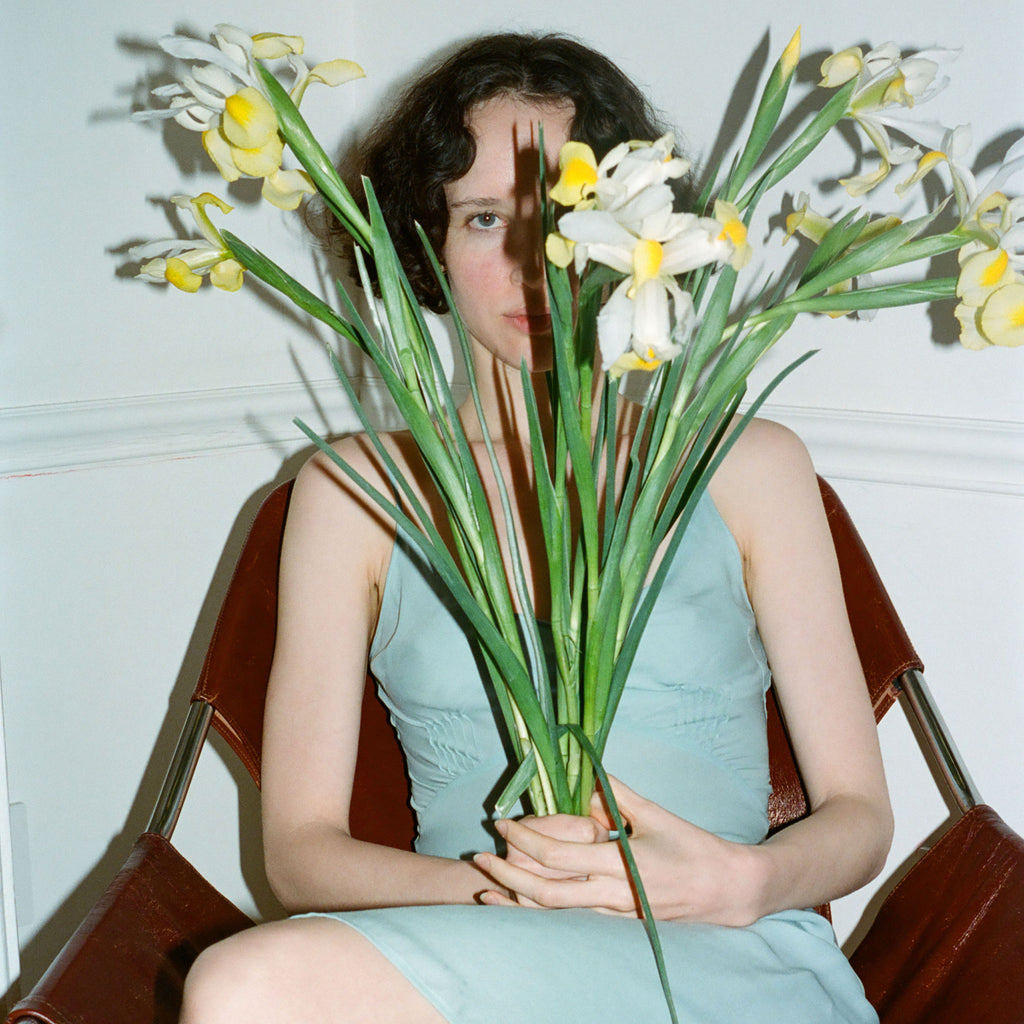 A model wearing the Cadel slip in pale blue, holding a bouquet of yellow flowers.