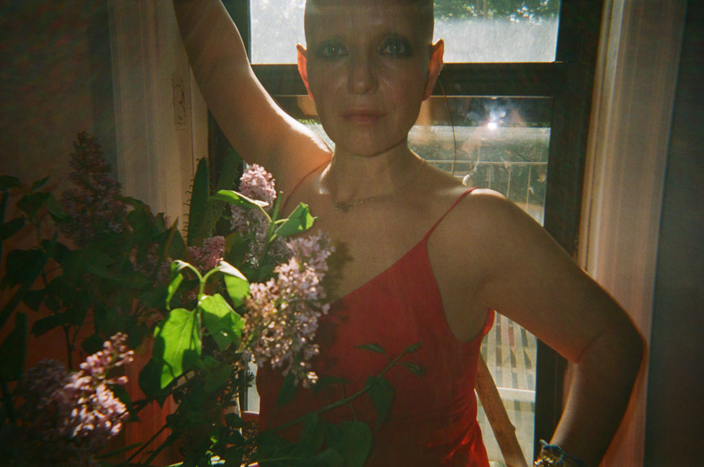 Woman in a red slip standing behind flowers.