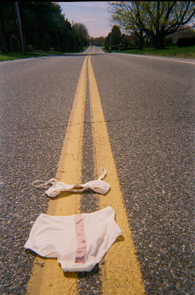 A pink bra and underwear laid in the middle of an empty road.