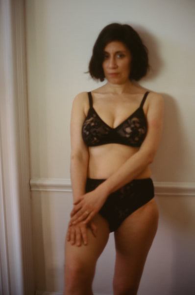 Araks wearing a black lace bra and underwear standing against a door.