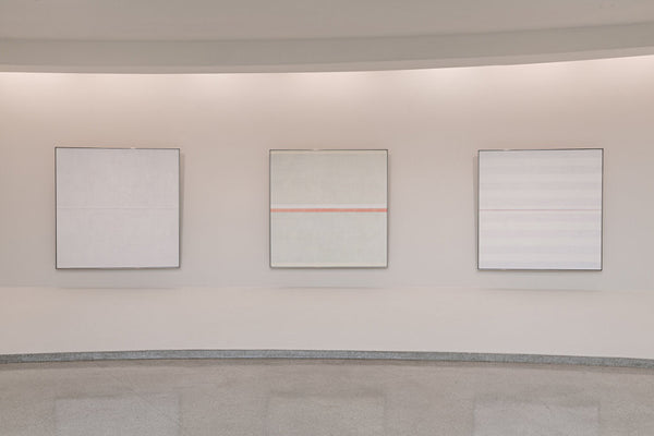 Three white paintings displayed on a blank wall.