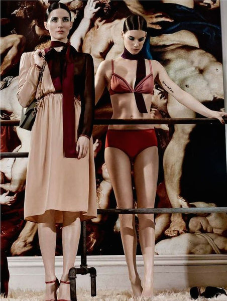 2 women standing. One in tan and red dress, the other woman in red bra and panty