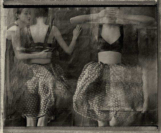 Black and white photograph of women in black bras and large polka dotted skirts.